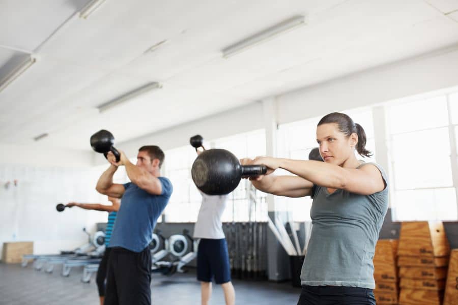 Group of people doing kettlebell swings in a gym, capturing the popularity of functional training in current exercise trends.