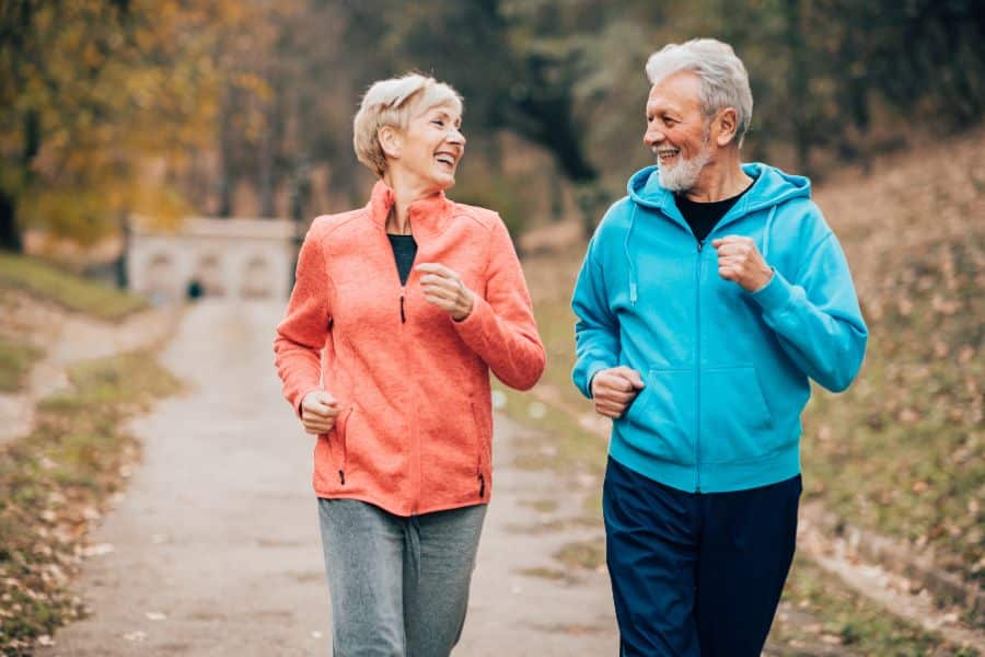 Older couple jogging outdoors in colorful activewear, illustrating the rise of walking and low-impact cardio in exercise trends.