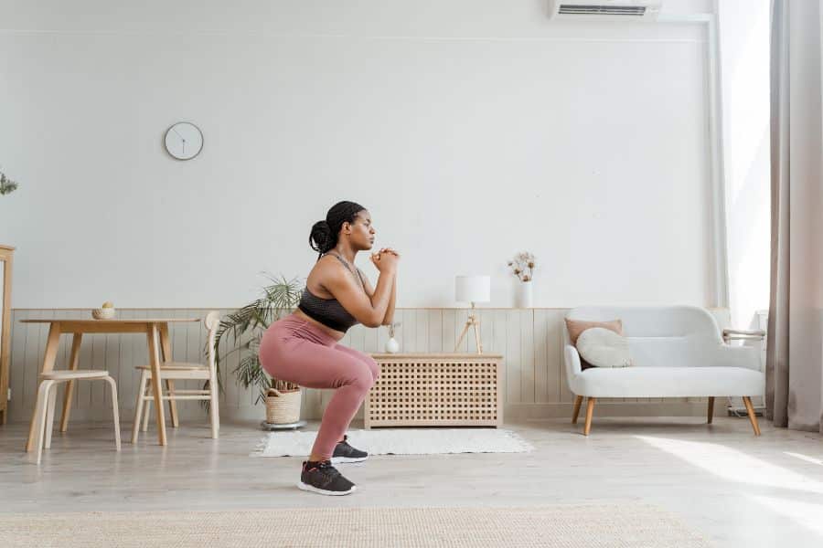 Woman doing bodyweight squats in a stylish home interior, reflecting the ongoing home workout boom in exercise trends.