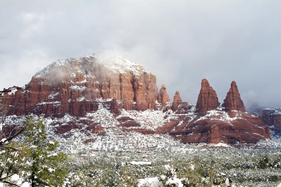 Snow covers the iconic red rock formations of Sedona, Arizona, with mist swirling around the cliffs. A unique winter RV trip stop blending desert landscapes and snow for a dramatic visual contrast.