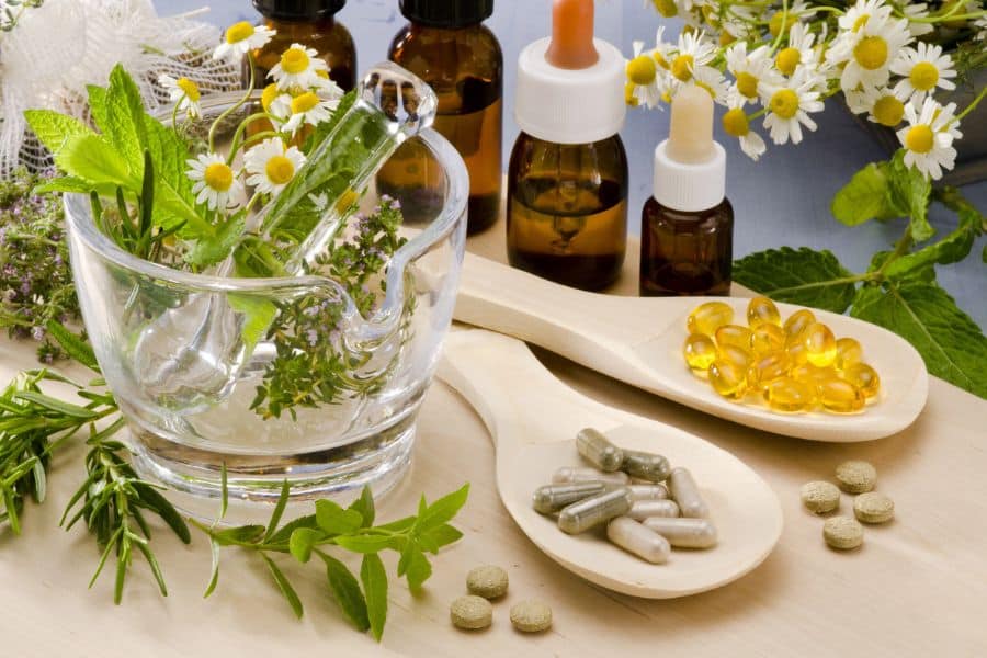 Herbal supplements and essential oils arranged with fresh herbs and flowers on a wooden table. Relying solely on natural remedies without professional advice is a frequent healthy habit mistake.