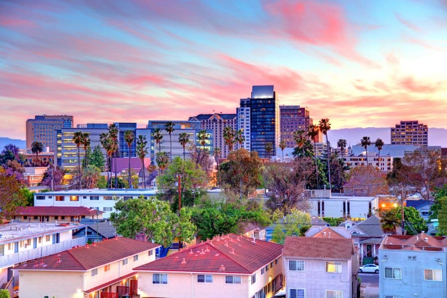 A colorful sunset over downtown San Jose, California, featuring palm trees and modern high-rises. While not abroad, this image contrasts with countries that welcome Americans for relocation or travel