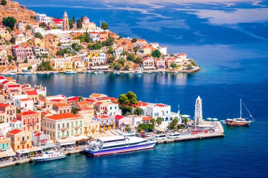 The island of Symi, Greece, with pastel-colored houses and boats docked along a deep blue harbor. Greece is one of the countries that welcome Americans, especially for extended stays.