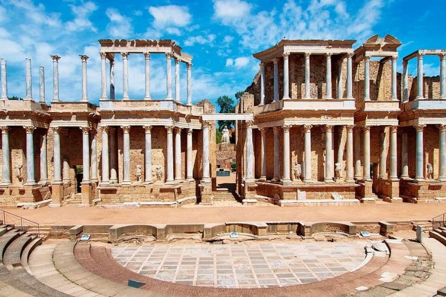 The Roman Theatre in Mérida, Spain, with towering white columns and ancient stone ruins standing under a bright blue sky. This UNESCO site invites travelers to embrace the cultural richness of slow travel destinations in Europe.