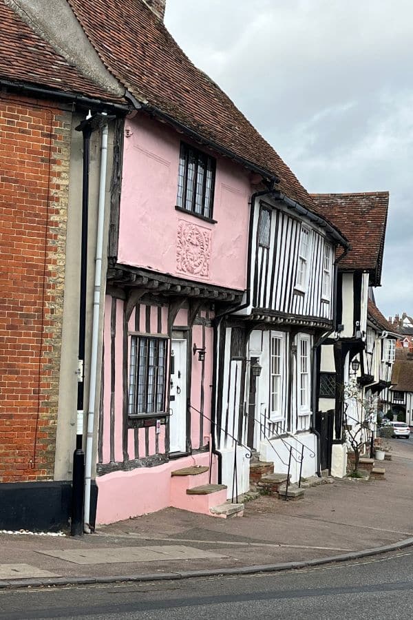 A pastel pink house with exposed beams and a crooked roof stands in a row of medieval homes typical of villages in Europe.