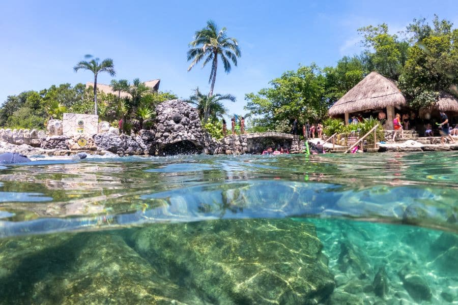 A split-level water view at Xcaret Park in Mexico, with clear turquoise water, stone structures, and palm trees above. Mexico is one of the closest and most accessible countries that welcome Americans for travel or living abroad.