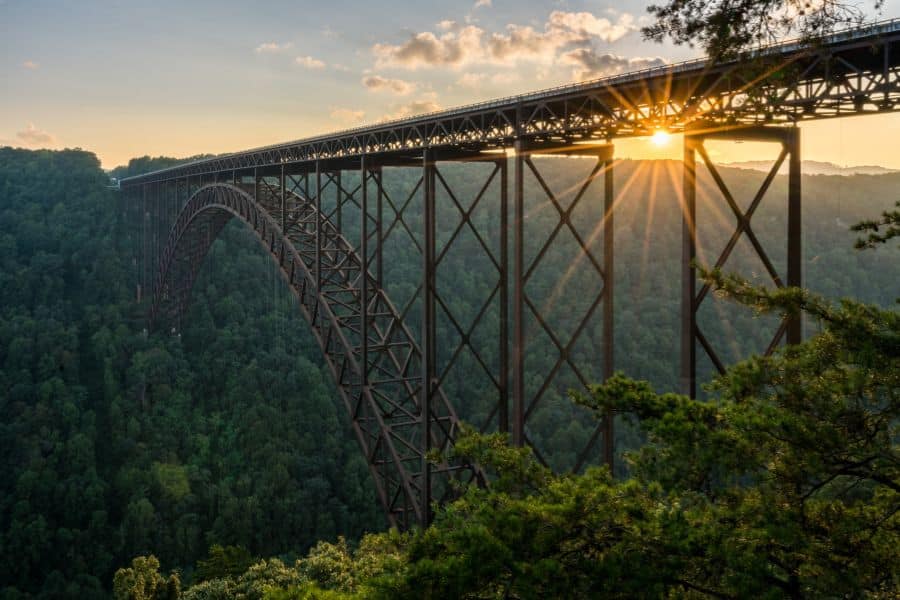 New River Gorge Bridge at sunset, its steel arch spanning a deep forested canyon with golden light filtering through. Though visually stunning, limited access points and seasonal traffic can make it one of the national parks to avoid during holidays.