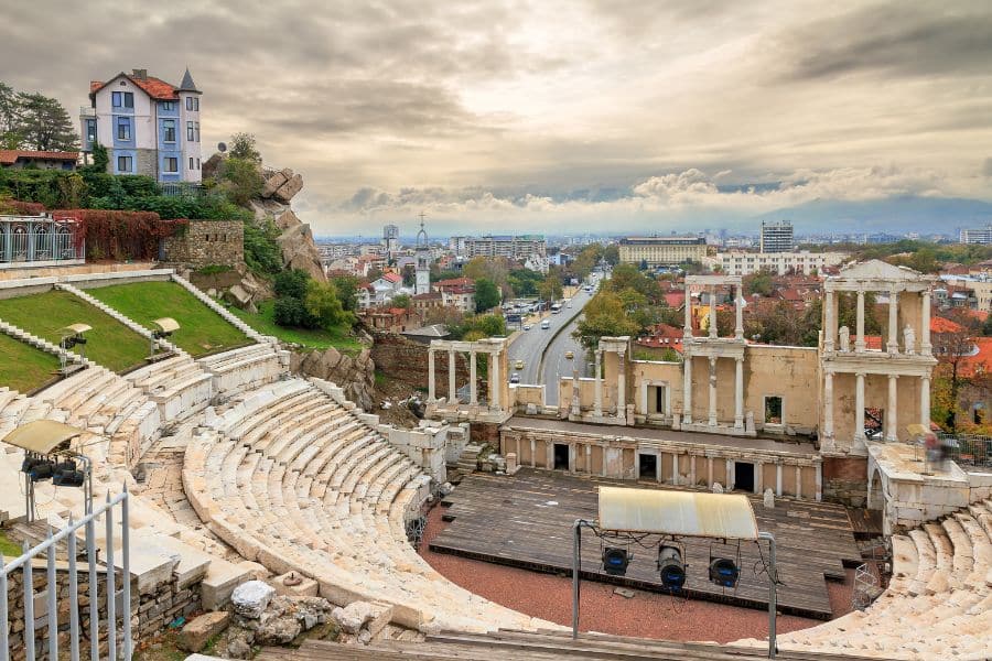 Plovdiv’s Roman amphitheater is in the foreground with a panoramic view of the modern city and distant mountains beyond. An affordable gem among towns in Europe where you can live for less while being surrounded by ancient history.