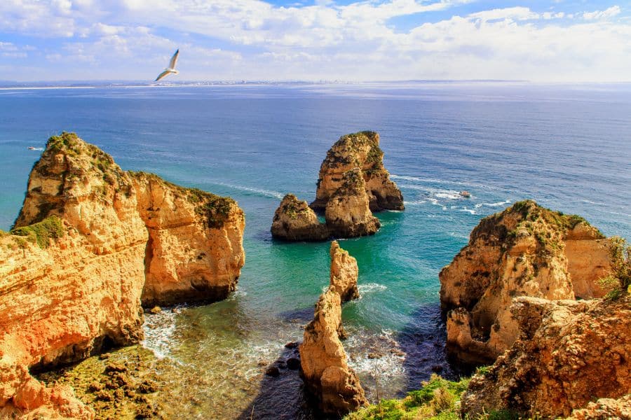 Dramatic coastal cliffs and sea stacks rise from the turquoise waters in Lagos, Portugal, with a seagull soaring above. Portugal remains high on the list of countries that welcome Americans due to its relaxed lifestyle and residency options.