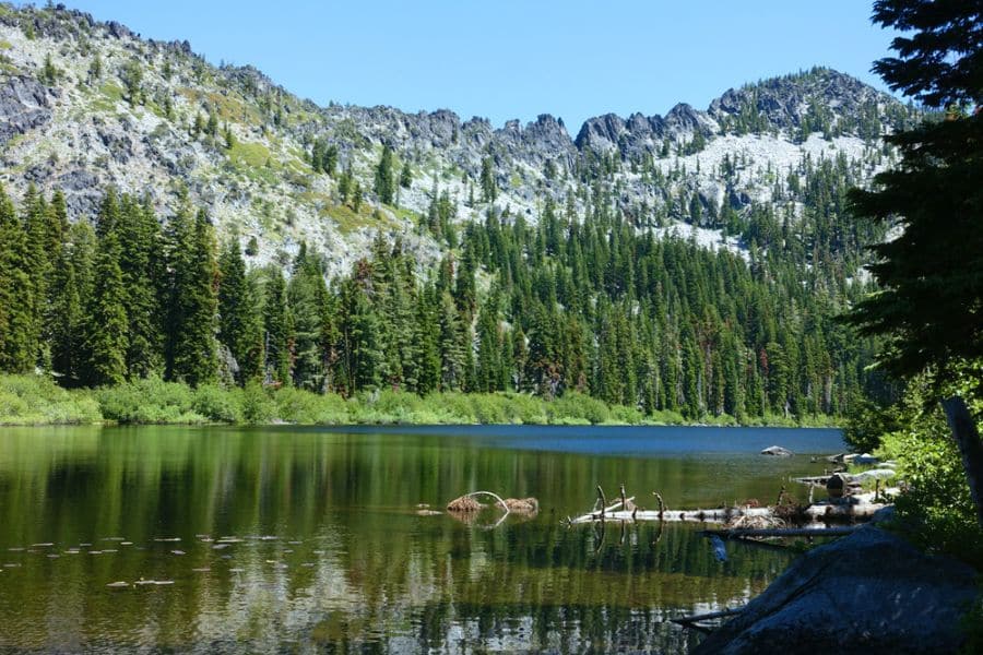A peaceful alpine lake reflects surrounding evergreens and rugged mountain peaks, showing the natural beauty that draws visitors to Overcrowded US National Parks.