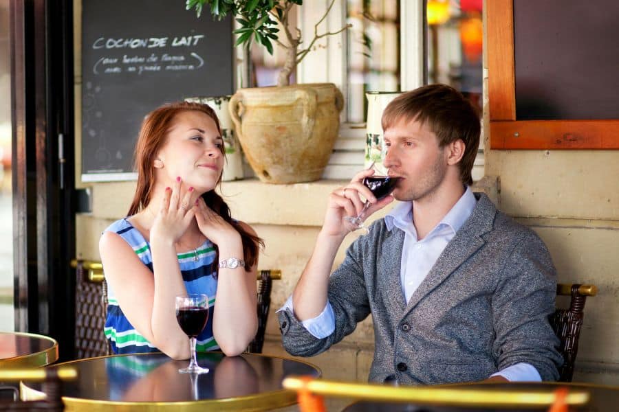 A smiling couple enjoying glasses of red wine at a Parisian café terrace, engaging in relaxed conversation. Scenes like this reflect the slower lifestyle often cited in discussions of why the French are living longer than the Americans.