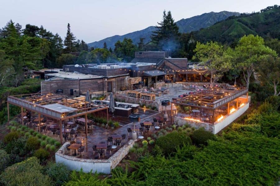 An expansive resort nestled in the hills features multiple outdoor dining areas with fire pits and lush greenery, representing elevated dining experiences at All-Inclusive Resorts in the US.