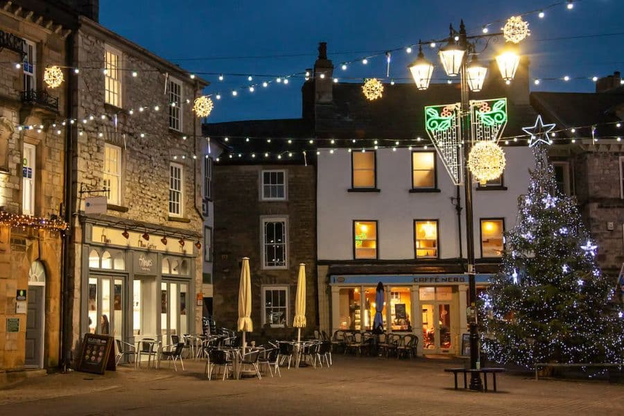 A festive town square illuminated by fairy lights and golden Christmas decorations, with a glowing tree and cozy cafés. This inviting setting is a great example of the twinkling town centers that make ideal places to visit at Christmas in the UK.