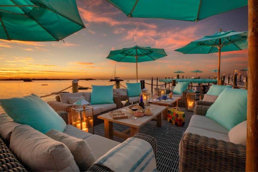 A cozy dockside lounge at sunset is set with turquoise umbrellas, lanterns, wine, and appetizers, capturing romantic dining at premium All-Inclusive Resorts in the US.