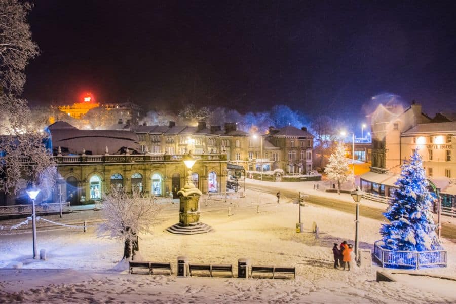 Buxton town center sparkles at night with snow-covered streets, Christmas trees lit in blue and white, and historic buildings all around. This Peak District gem is one of the scenic places to visit at Christmas in the UK.