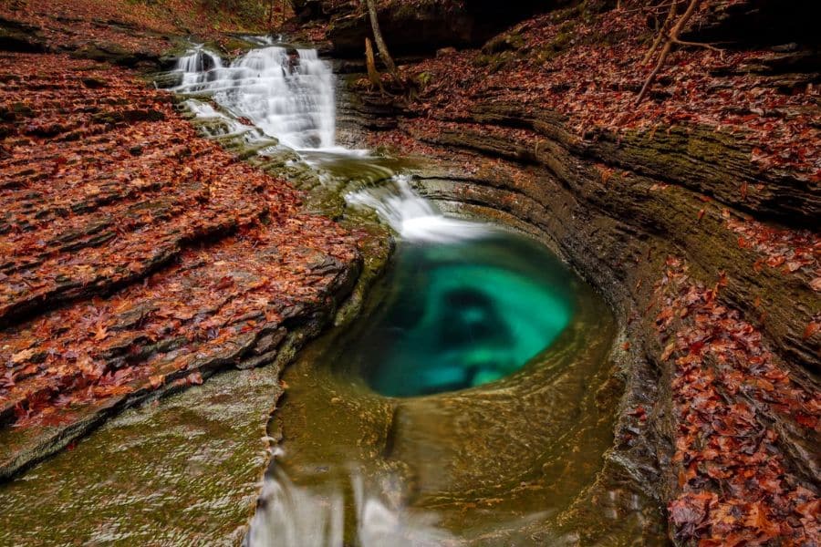 Vibrant green plunge pool beneath a cascading waterfall in a narrow rocky gorge, a hidden gem among America’s Best-Kept Hiking Secrets found in the Finger Lakes region.