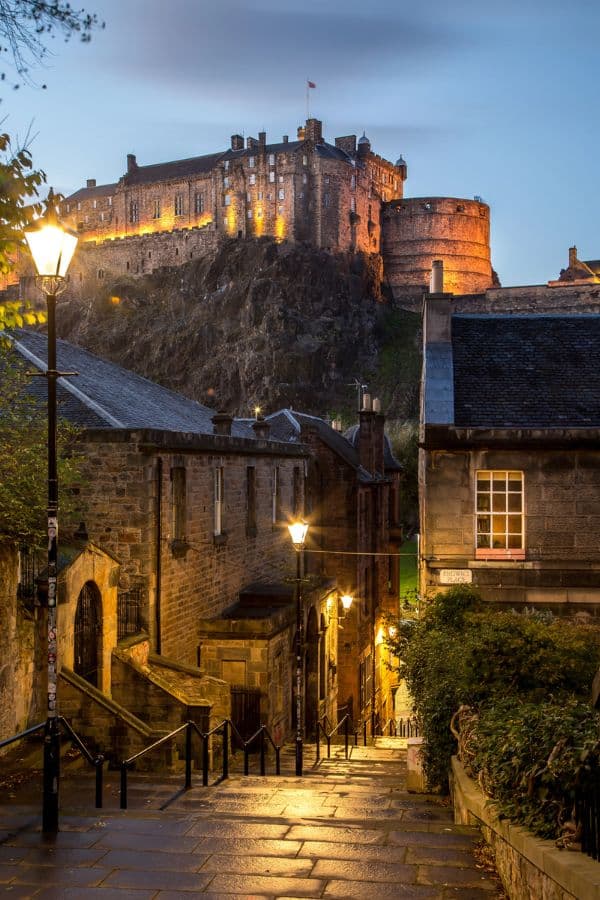 A cobblestone street leading to the illuminated Edinburgh Castle at dusk, offering a magical perspective on one of the top Medieval Places to Visit in Europe.