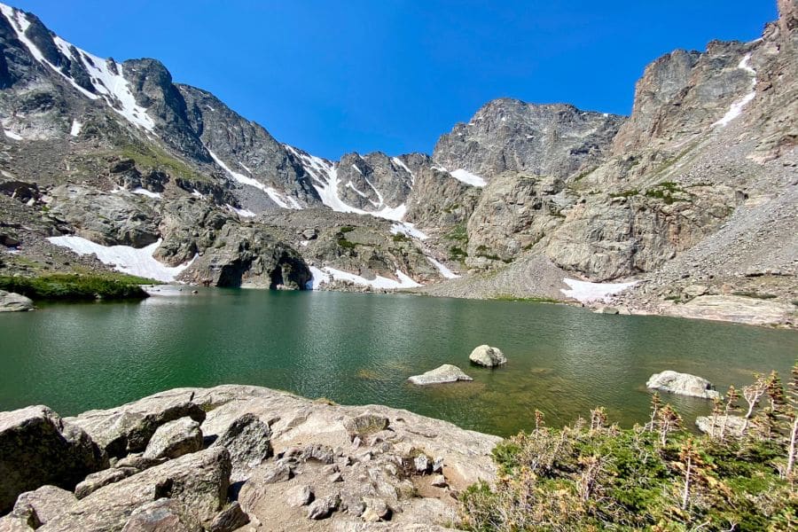 Glacial lake at the base of steep, rugged mountains with scattered snow patches, an untouched example of America’s Best-Kept Hiking Secrets in the Rockies.