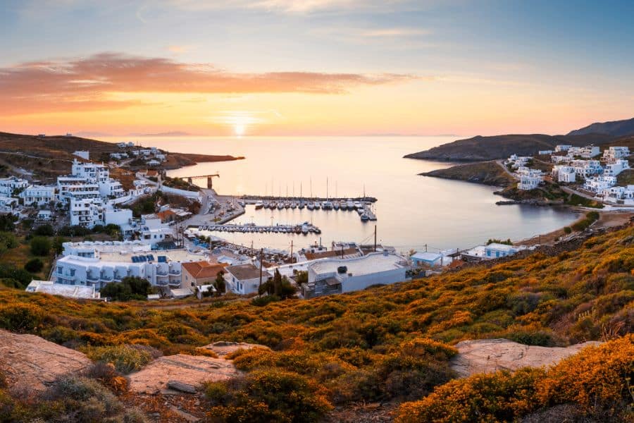A peaceful harbor on a Greek island at sunset, with sailboats docked and whitewashed buildings nestled on hillsides. This serene setting offers an ideal retreat to escape the winter blues in January with island calm and warmth.