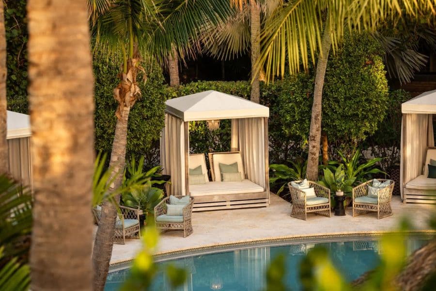 Poolside cabanas and wicker lounge seating are tucked among palm trees and greenery, creating a serene tropical retreat at All-Inclusive Resorts in the US.