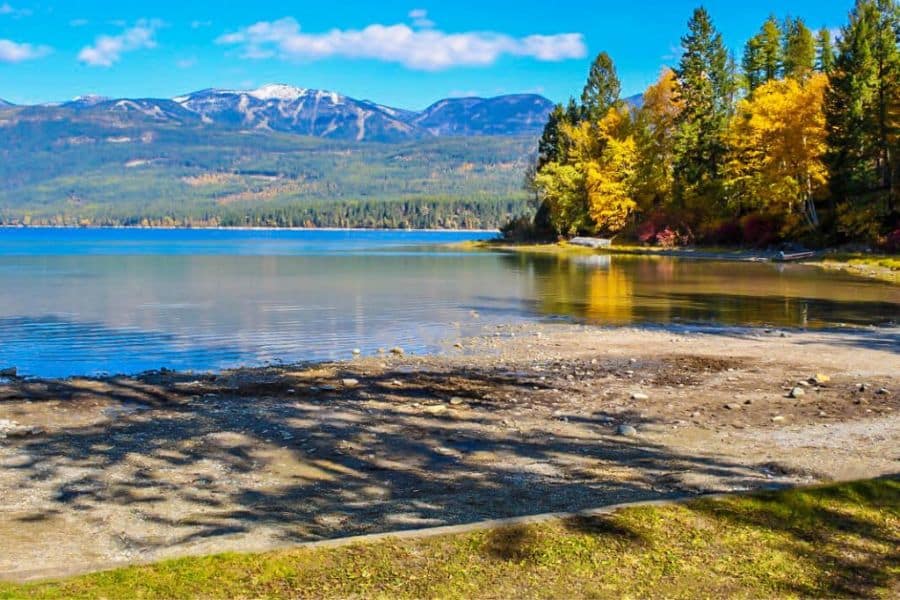 Bright fall foliage lines the shore of a calm lake with distant mountains, a typical serene view now often sought in Overcrowded US National Parks.