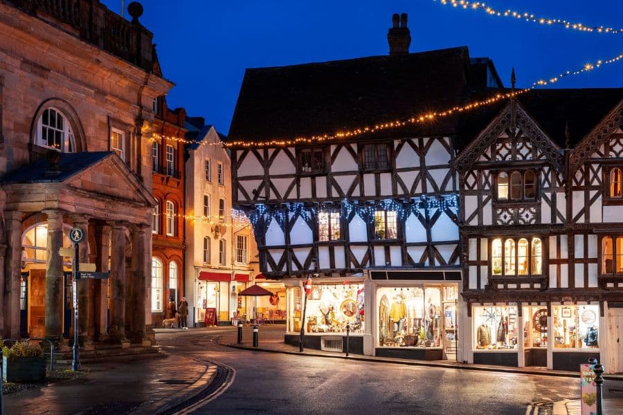 A Tudor-style building in Ludlow is decorated with Christmas lights, with shop windows glowing along the cobbled street. Historic towns like this make for atmospheric places to visit at Christmas in the UK.
