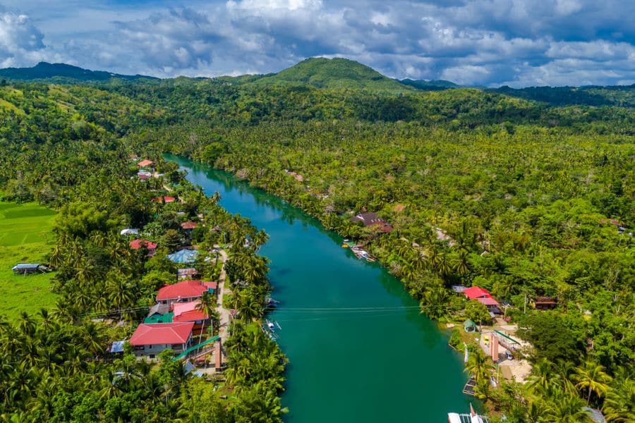 Aerial view of a vibrant village along a winding river surrounded by tropical forest, a scenic destination accessible when you Live on a Cruise Ship.