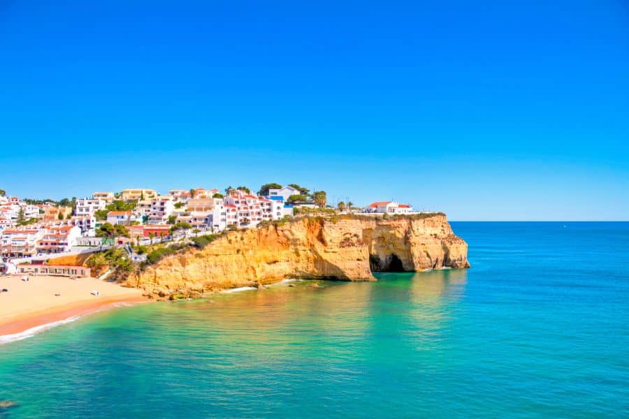 Colorful cliffside homes and golden beaches of a Portuguese coastal town, showing the charming ports of call you can explore when you Live on a Cruise Ship.