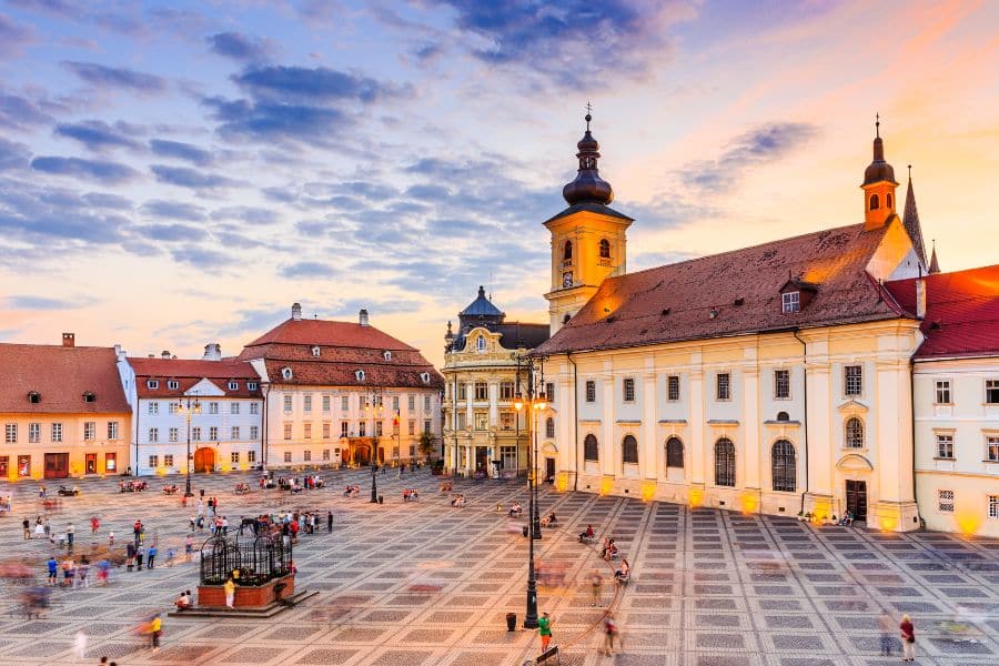 Evening scene in Sibiu’s historic central square with illuminated baroque buildings and a soft sunset sky, highlighting why Romania is one of the best cheap places to visit in Europe.