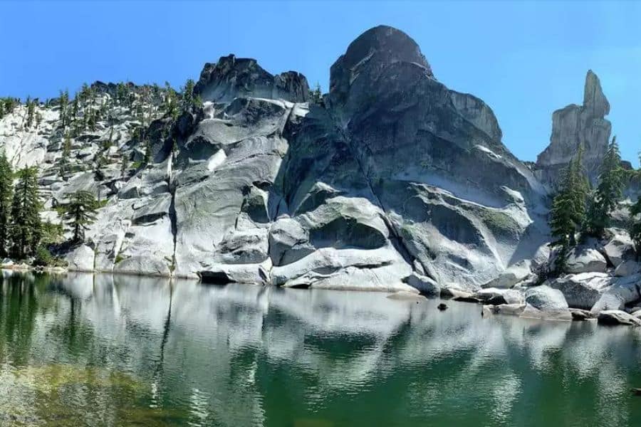 Jagged granite cliffs tower over a still lake with pine trees at the edges, capturing the dramatic scenes that contribute to Overcrowded US National Parks.