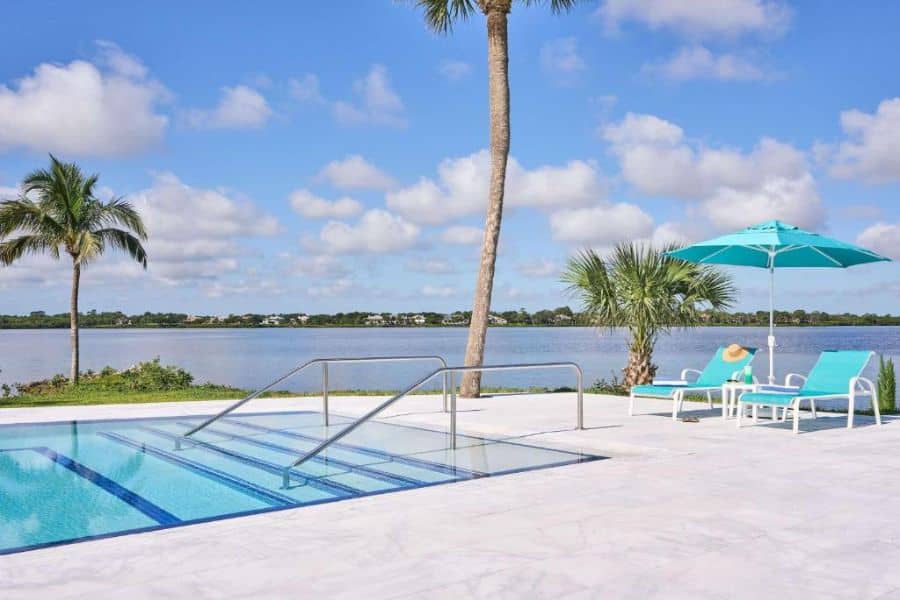 A minimalist resort pool with aqua lounge chairs and umbrellas overlooks a calm waterway, offering peaceful views at one of the relaxing All-Inclusive Resorts in the US.