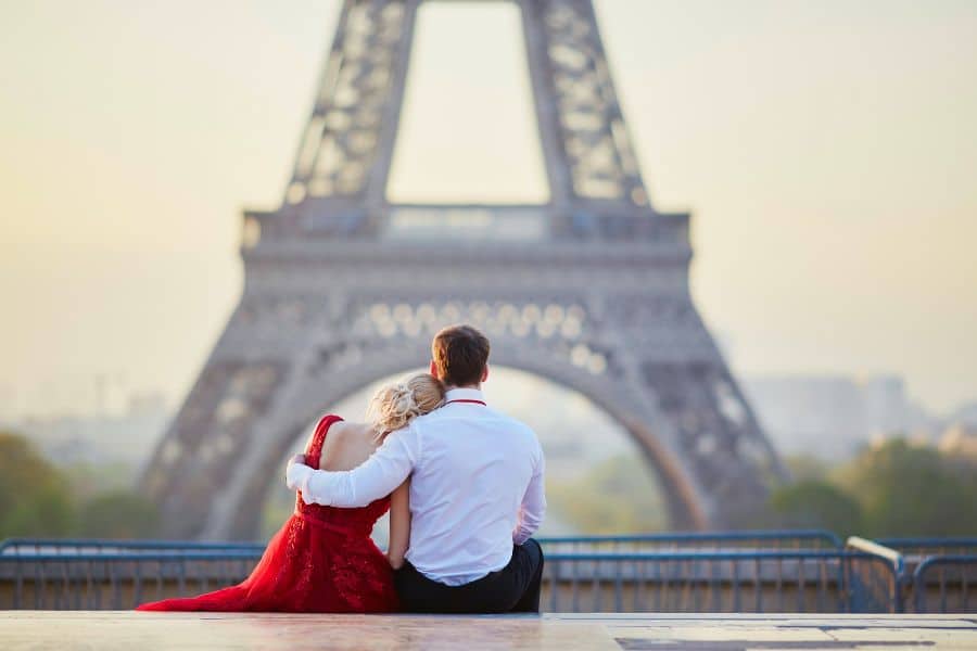 A couple sits arm-in-arm gazing at the Eiffel Tower, embracing a peaceful moment. Strong social ties and low-stress lifestyles contribute to why the French are living longer than the Americans.