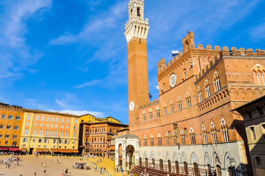 The Torre del Mangia in Siena, Italy, towers over Piazza del Campo with its distinctive red brick facade and clock tower, standing out among the grand Medieval Places to Visit in Europe.