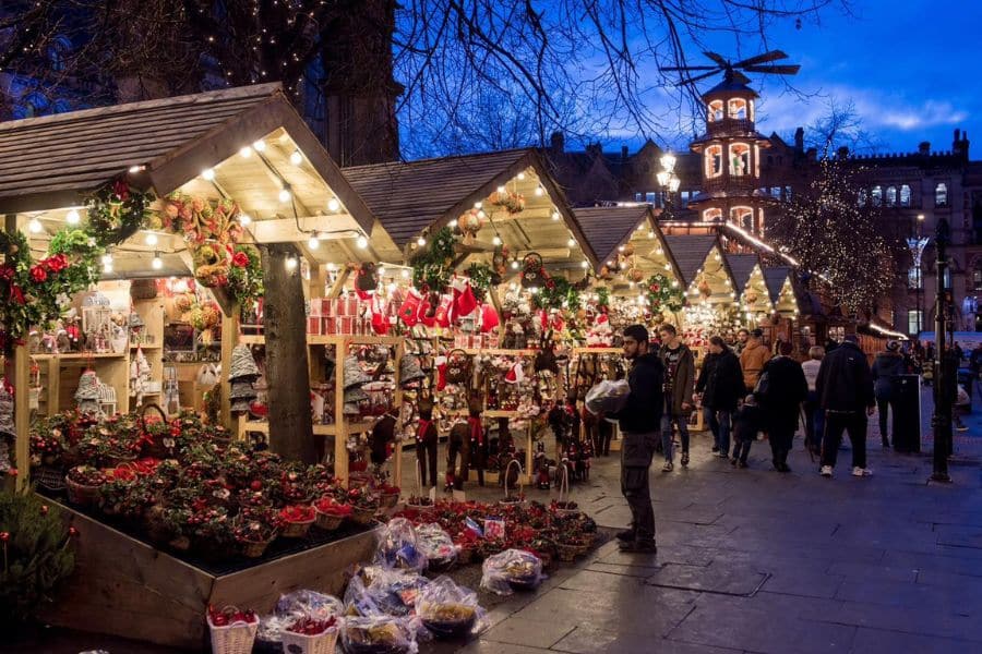 A bustling Christmas market in Skipton features wooden stalls filled with festive gifts and decorations, glowing under string lights. Traditional markets like this are among the top places to visit at Christmas in the UK for seasonal cheer.