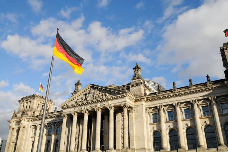 The Reichstag building in Berlin, Germany, with the German flag waving under a blue sky—highlighting a location where US credit cards don’t work in this European city due to cash-preferred culture.