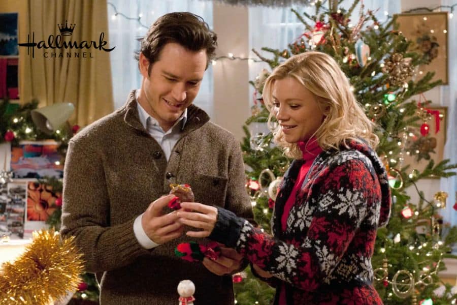 A man and woman with a ring box stood in front of a Christmas tree
