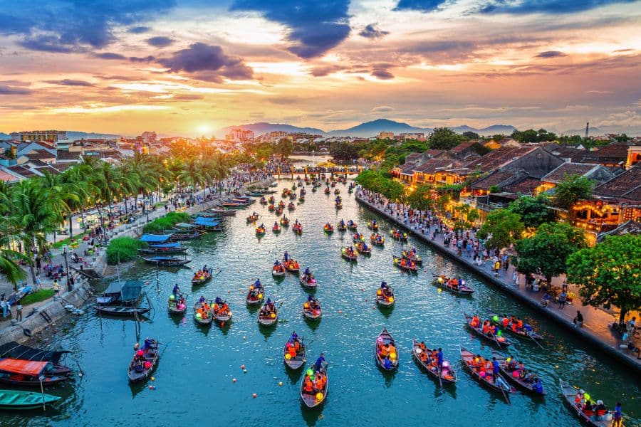 Dozens of lantern-lit boats float along a vibrant canal at sunset in Hoi An, Vietnam, a magical moment you might experience when you Live on a Cruise Ship.
