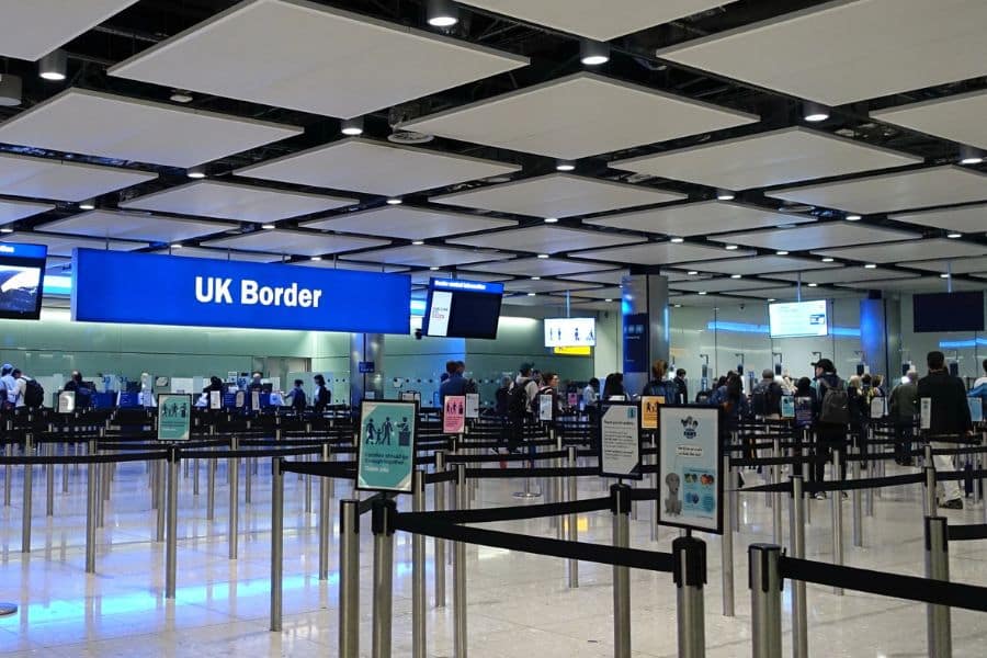 Busy UK airport border control area with signage reading "UK Border," showing travelers lining up, reflecting the enforcement of the New UK Travel Rules at entry points.