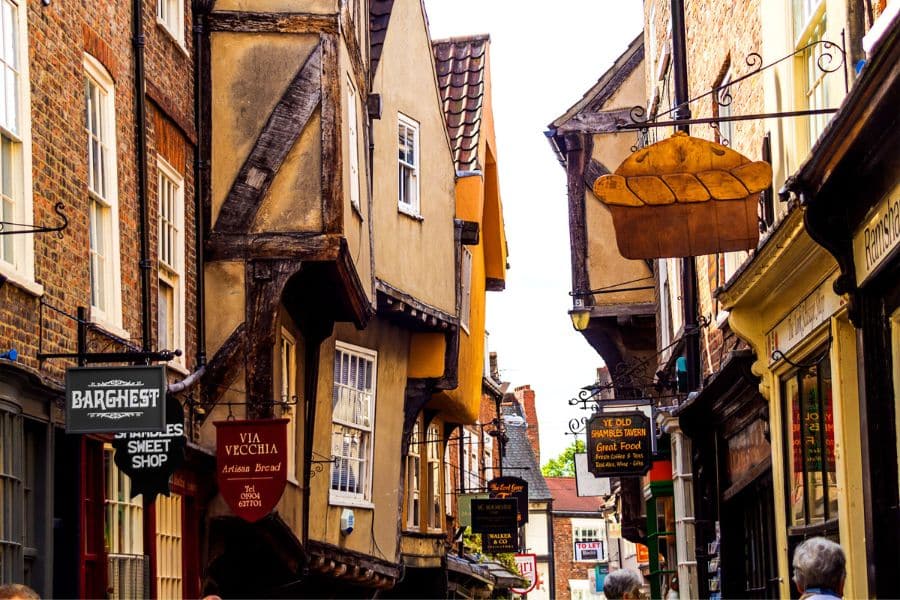 A closer daytime view of The Shambles in York, England, with hanging shop signs and overhanging upper floors, showing why it's one of the most photographed Medieval Places to Visit in Europe.