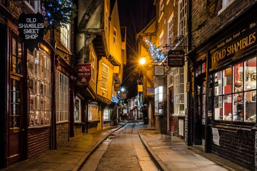 The Shambles in York lit up at night with festive lights and decorated shopfronts, creating a cozy Dickensian vibe. This historic street is one of the most enchanting places to visit at Christmas in the UK.
