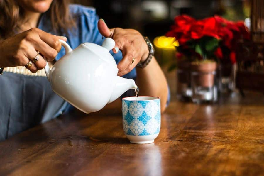 A woman hands pouring tea from a white teapot into a mug