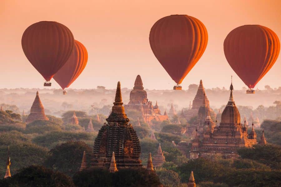 Hot air balloons drift above ancient pagodas at sunrise in Bagan, Myanmar. This magical scene places Bagan among the world's top Bucket List Destinations to Visit.
