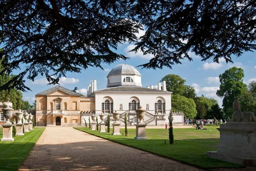 Neoclassical building with a domed roof, statues, and symmetrical design surrounded by lush greenery and visitors. This site is another notable Bridgerton location often used for garden or promenade scenes.