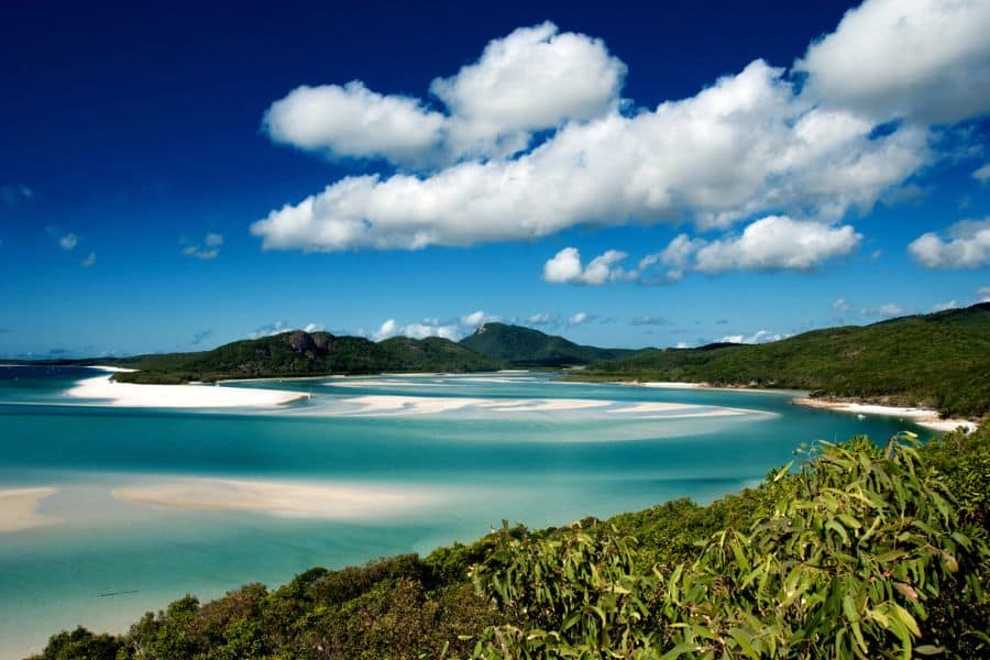 Whitehaven Beach in Australia stretches across swirling turquoise waters and white sandbanks under a blue sky. This pristine shoreline is a standout among Bucket List Destinations to Visit.
