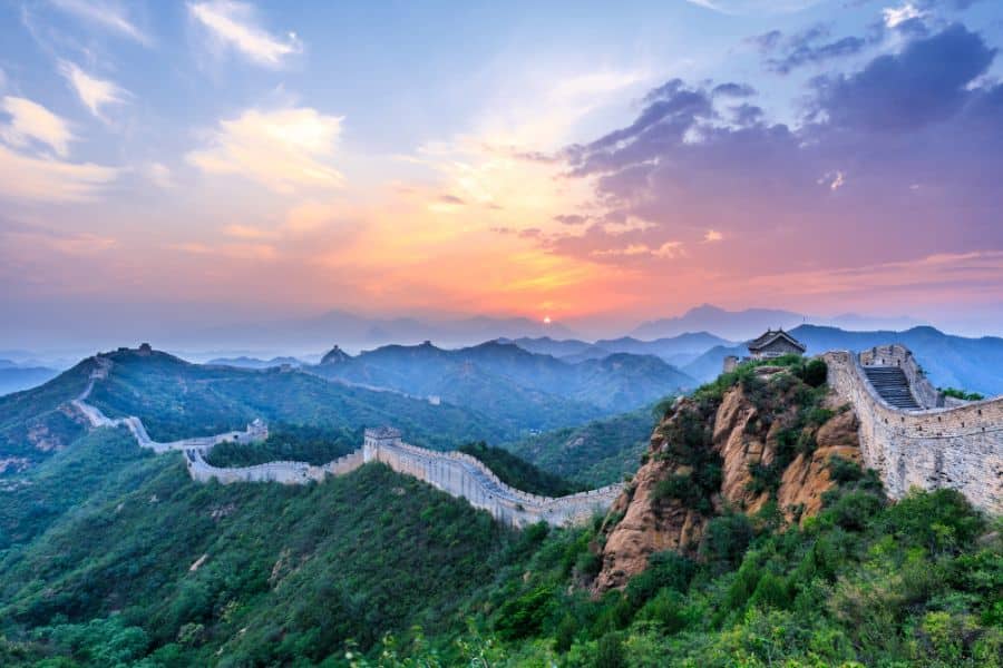 The Great Wall of China winds over green mountains during a colorful sunset. As one of the world’s wonders, it’s firmly among the top Bucket List Destinations to Visit.