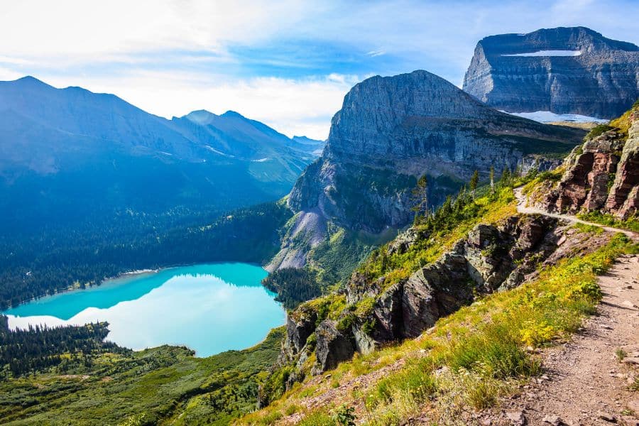 A vivid turquoise lake lies below a dramatic mountain backdrop along the Grinnell Glacier Trail in Glacier National Park, Montana. A stunning example of alpine hiking trails in the US.
