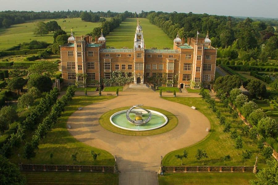 Aerial view of Hatfield House with formal gardens, a circular driveway, and symmetrical layout surrounded by woodlands. Its stately appearance makes it one of the prominent Bridgerton locations for grand estate scenes.