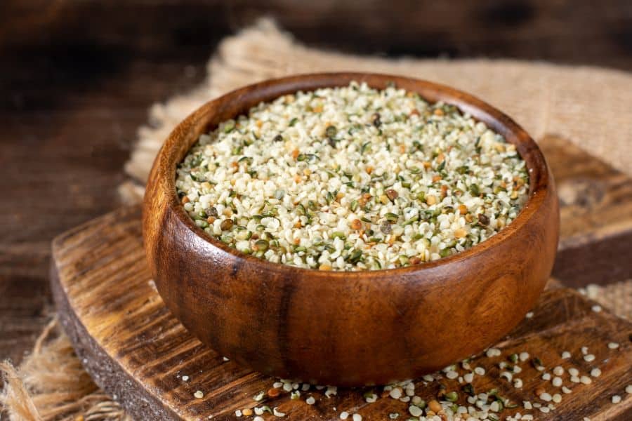 A wooden bowl filled with hulled hemp seeds, placed on a rustic surface. Hemp seeds are packed with omega-3s, making them one of the 7 Foods That Actively Fight Wrinkles.