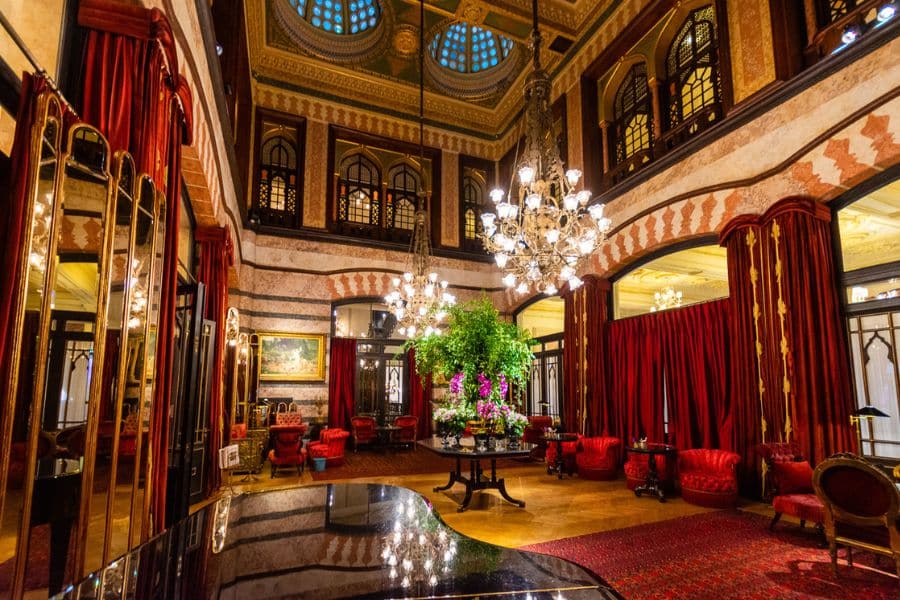 Ornate hotel lobby with grand chandeliers, lush red curtains, and high ceilings, showcasing the opulence of European Hotels Where Famous Writers Lived.
