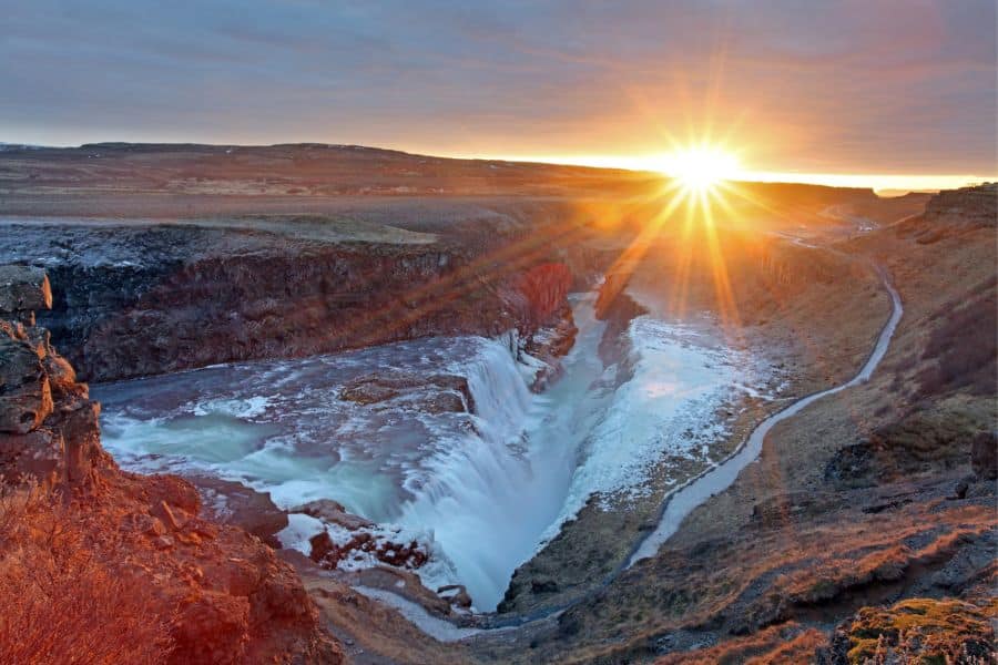 The sun rises over Gullfoss waterfall in Iceland, casting a golden glow on icy cliffs and roaring waters. This breathtaking natural wonder is one of the top Bucket List Destinations to Visit for adventure seekers.